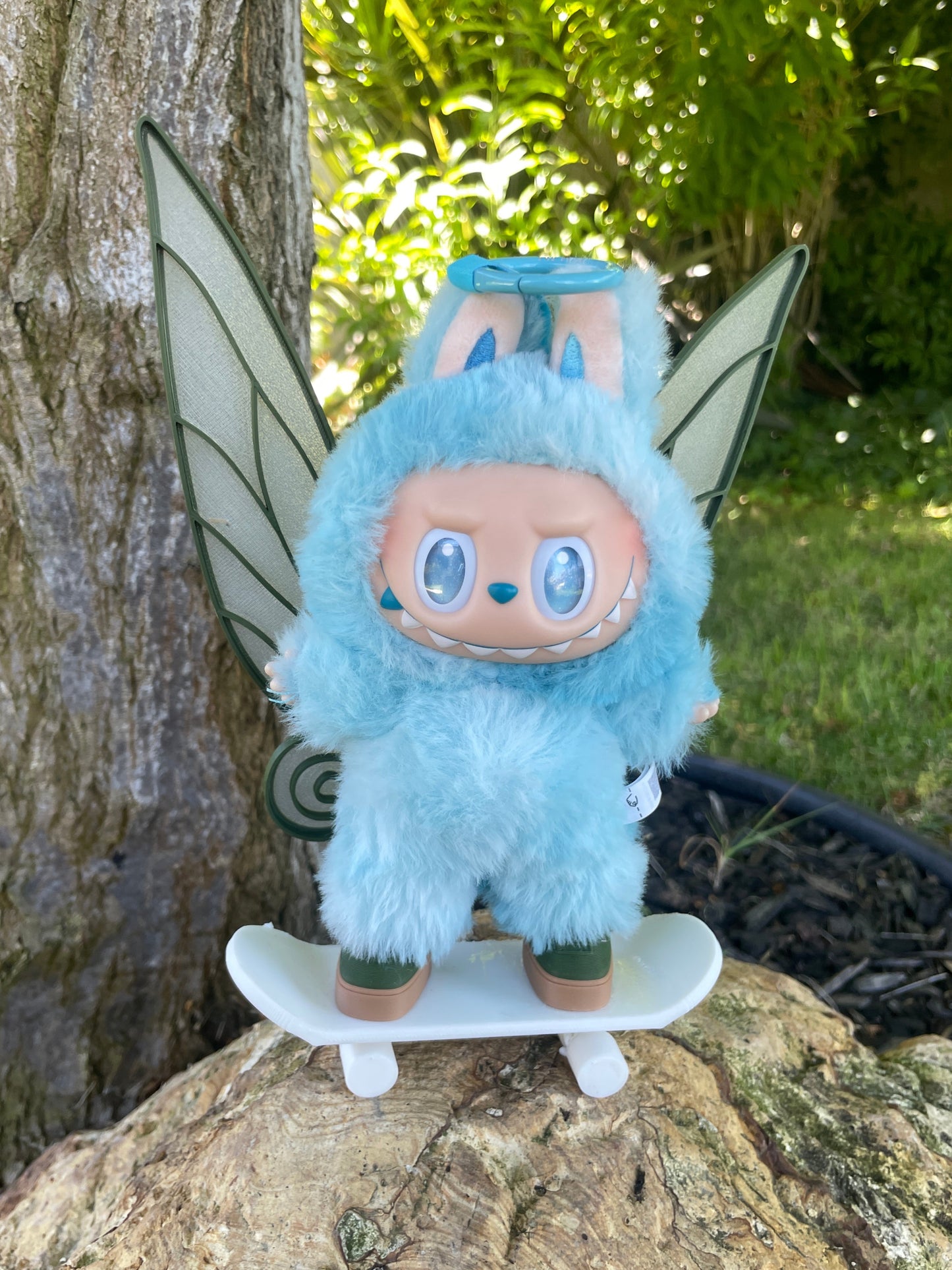 Blue fairy plush toy on a tree branch with greenery in the background